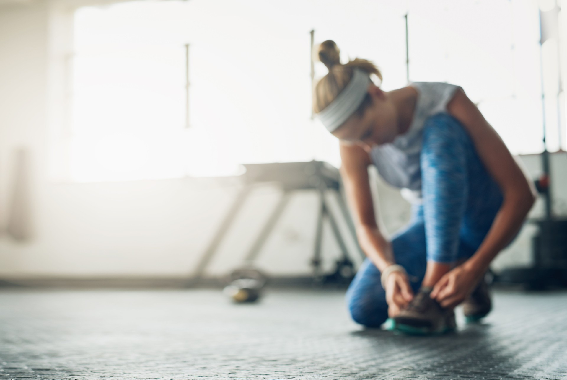 Mujer atándose las zapatillas en un gimnasio, lista para entrenar. Únete a nuestro programa de 8 semanas de nutrición y entrenamiento para transformar tu cuerpo y tu salud.