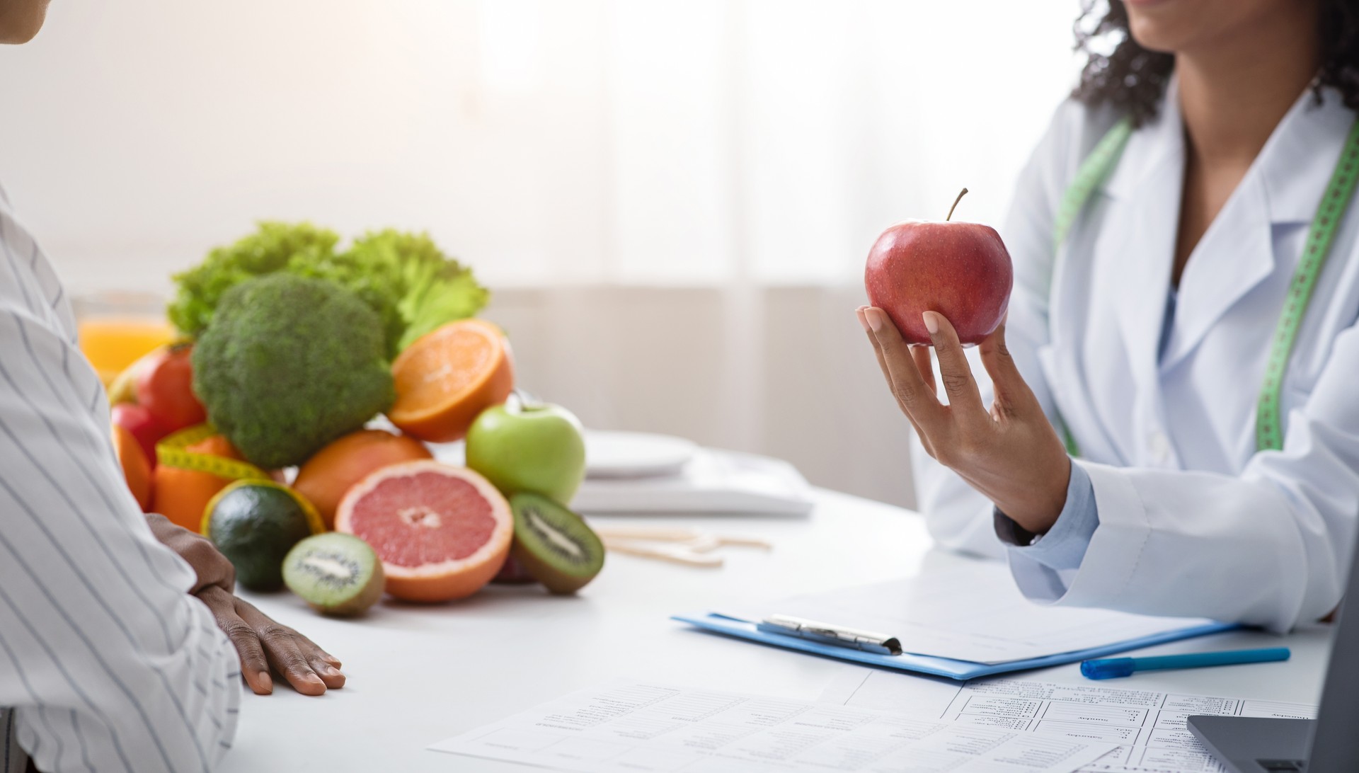 Recortado de nutricionista sosteniendo manzana roja frente al paciente