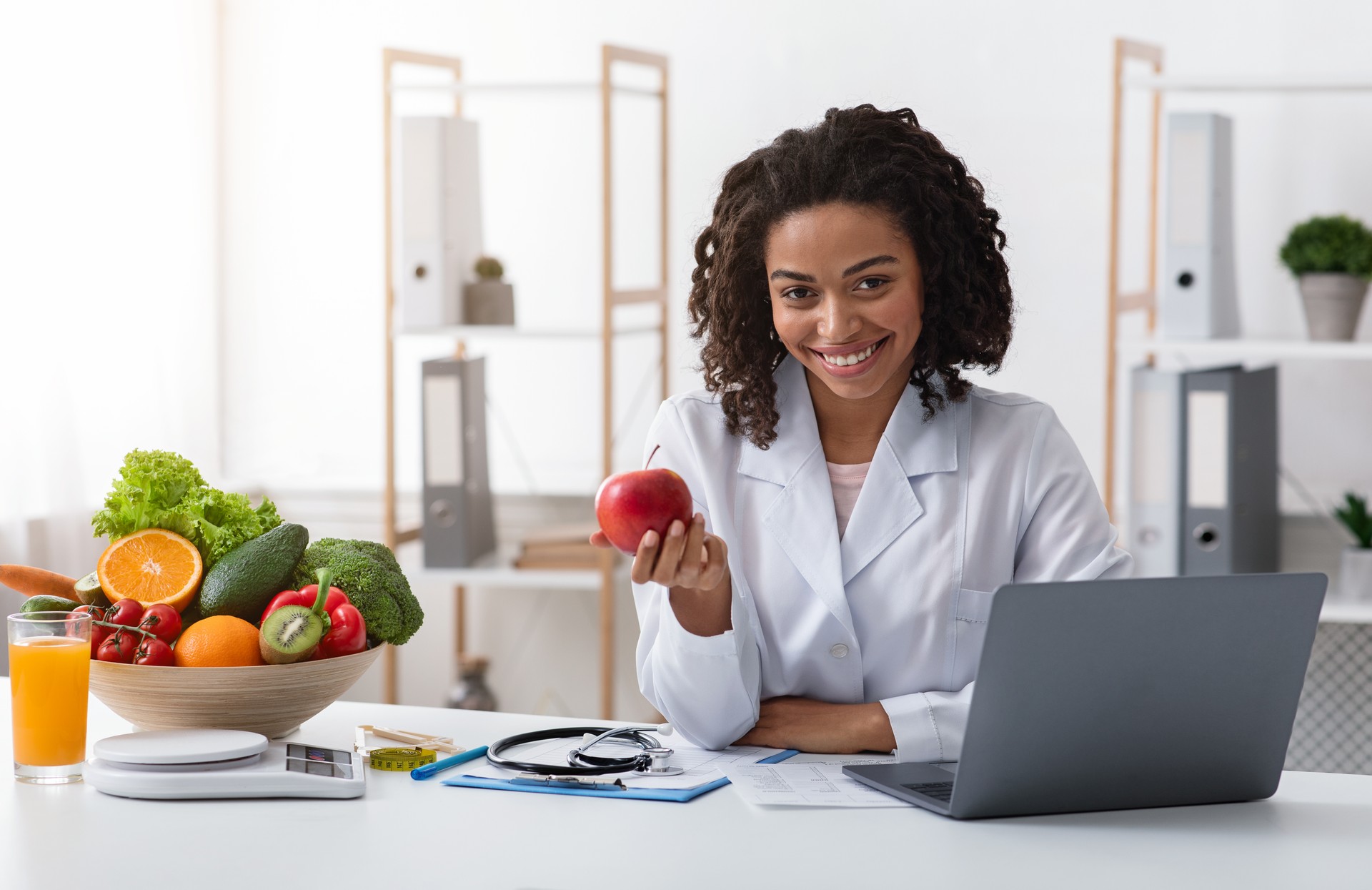 Atractiva mujer doctor amablemente recomendando comer frutas frescas